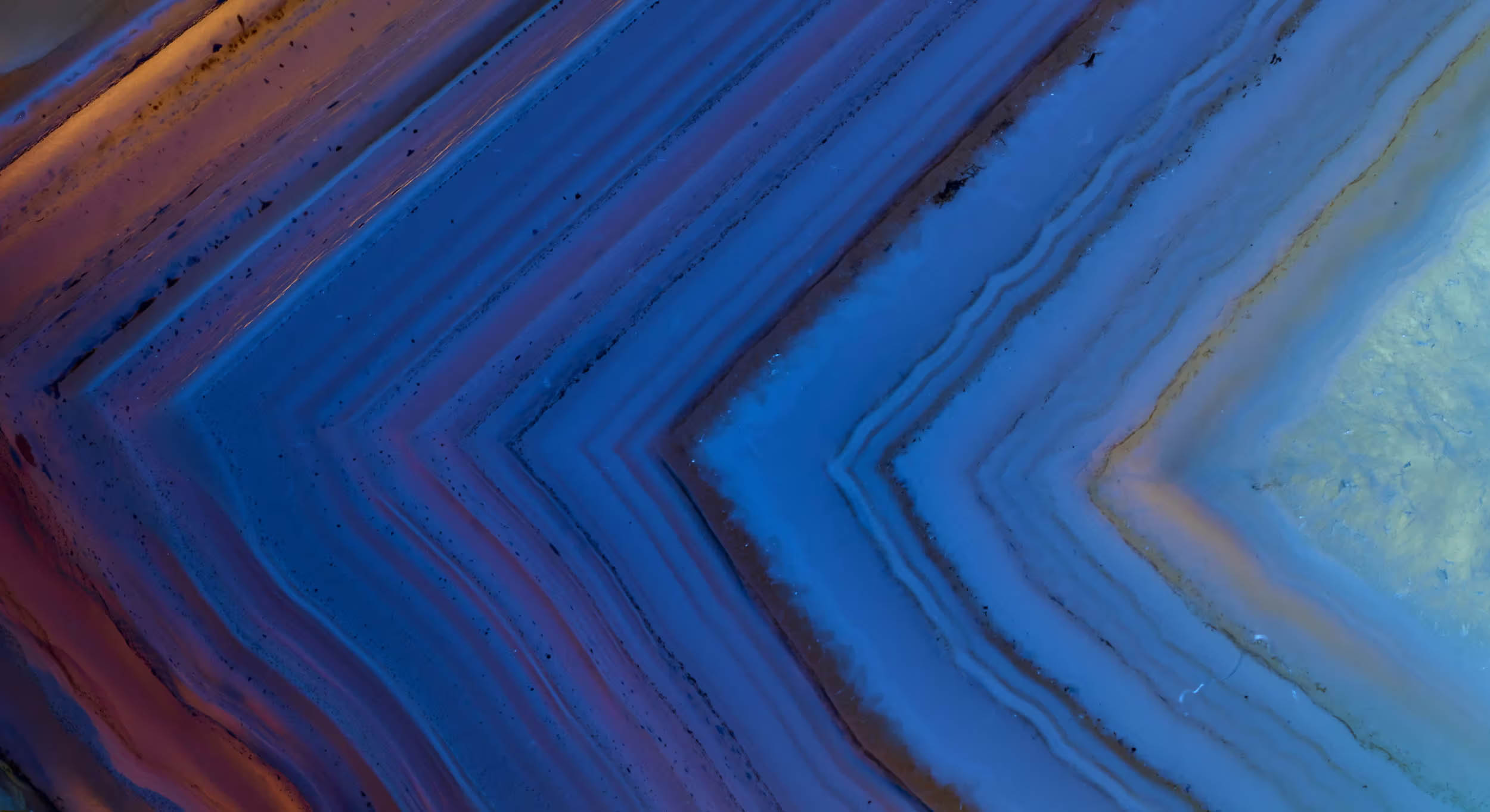 Close-up of blue and purple banded agate stone with sharp triangular layers and subtle orange highlights.